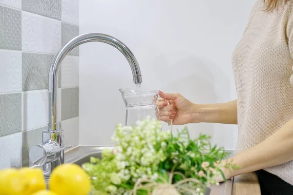 Женщина наливает воду в кувшин из кухонного крана — стоковое фото