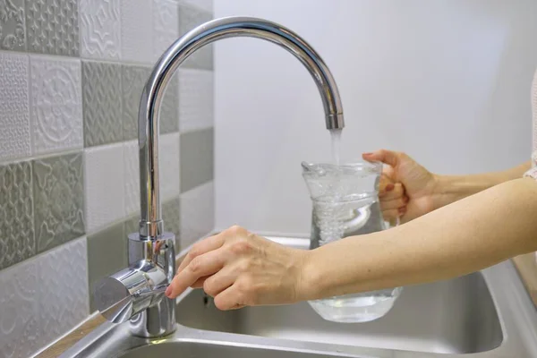 Mujer vertiendo agua en la jarra del grifo de la cocina — Foto de Stock