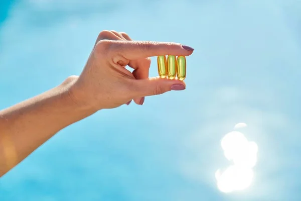 Cápsulas de aceite de vitamina D dorada soleada Omega-3 en mano mujer — Foto de Stock