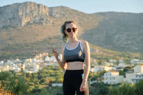 Teenager fitness runner girl with smartphone in earphones on mountain road — Stockfoto