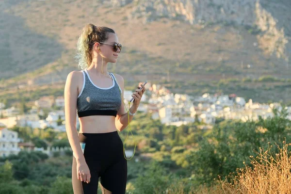 Tiener fitness runner meisje met smartphone in oortjes op de berg weg — Stockfoto