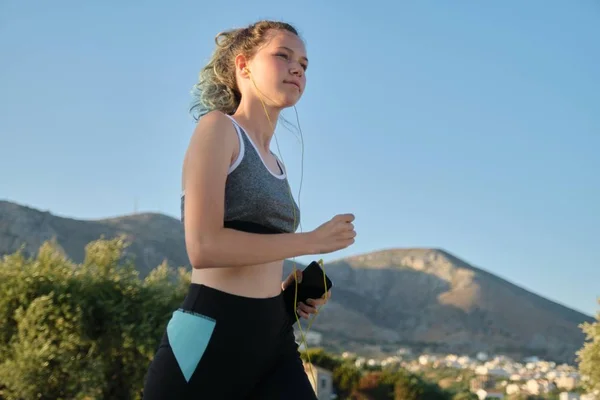 Running young teenager girl in fitness clothes headphones with smartphone — Stockfoto