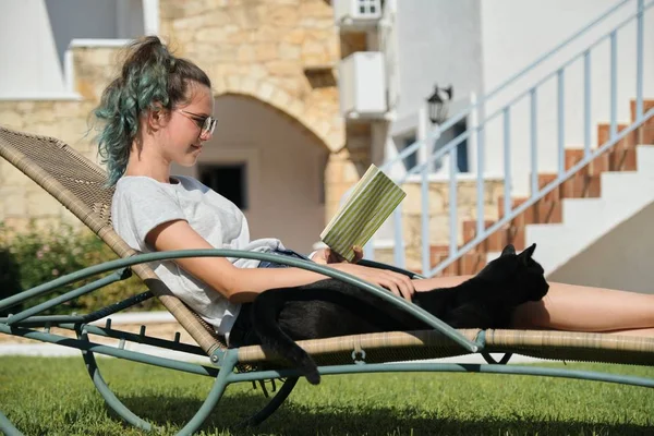 Rusten tiener meisje lezen boek met zwart huishoudelijk kat — Stockfoto