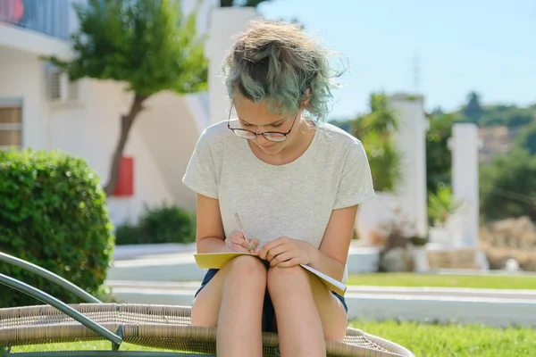 Studentka sedí venku, píše do školního sešitu — Stock fotografie