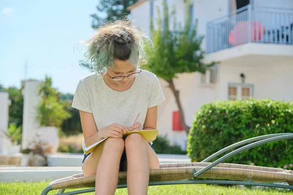 Studentka sedí venku, píše do školního sešitu — Stock fotografie