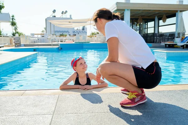 Deportiva niña en traje de baño gorra gafas en la piscina hablando con la madre —  Fotos de Stock