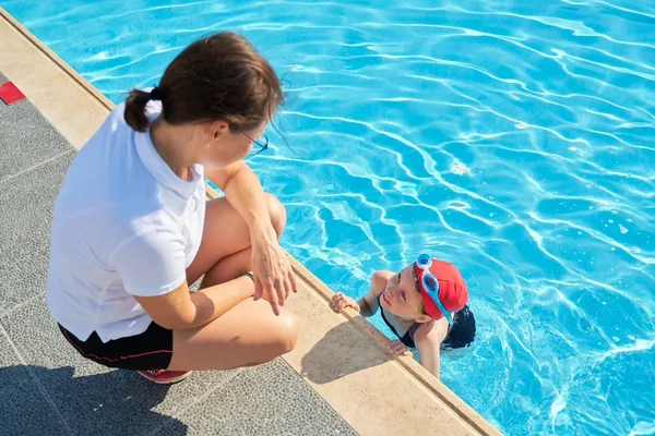 Mujer entrenador hablando con niña niño en traje de baño sombrero y gafas cerca de la piscina al aire libre —  Fotos de Stock