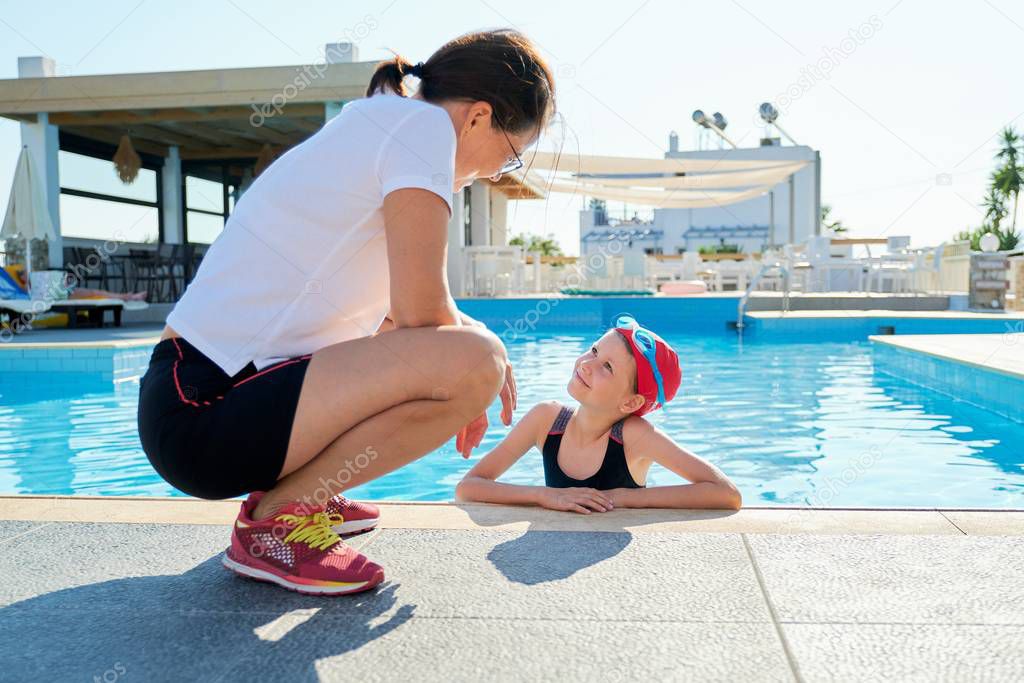 Sports girl child in swimsuit cap glasses in pool talking with mother