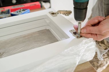 Mobilya montajı, yakın çekim, profesyonel aletlerle krom kapaklı kapı menteşeleri.