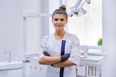 Kendine güvenen genç bir dişçinin portresi. Doktor kadın, kollarını kavuşturmuş.
