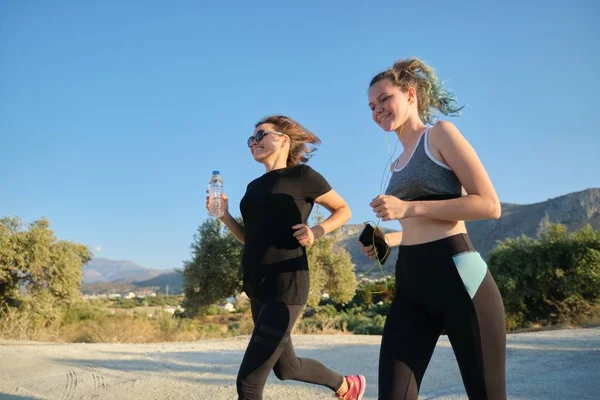 Middelbare leeftijd moeder en tienerdochter running outdoor — Stockfoto