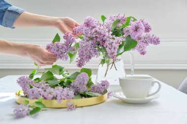 Kadın elleri cam sürahide leylak çiçekleriyle dolu