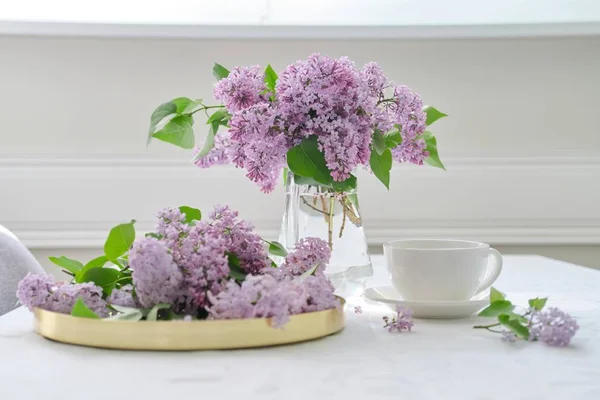 Ramo de flores de primavera de color lila en jarra de vidrio en la mesa, taza de té — Foto de Stock