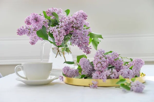 Ramo de flores de primavera de color lila en jarra de vidrio en la mesa, taza de té — Foto de Stock