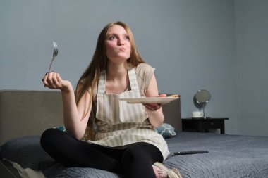 İlgilenen genç ve güzel bir kadın TV izliyor ve yemek yiyor.