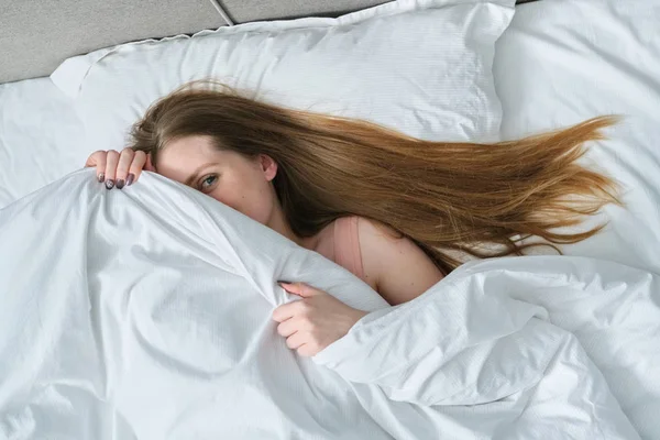 Обличчя молодої красивої жінки лежить на подушці в ліжку з ковдрою — стокове фото