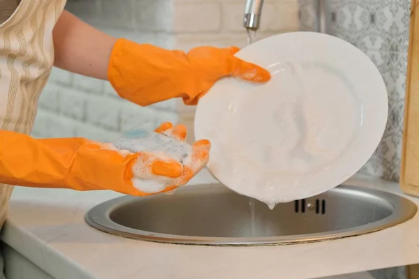 Gros plan des mains de la femme dans les gants laver la vaisselle dans la cuisine — Photo