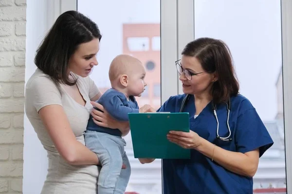 Посетить мать с ребенком в больнице, говорить педиатр врач и молодая женщина — стоковое фото