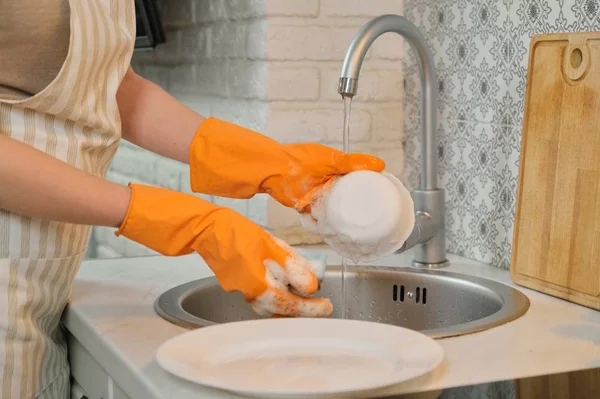 Mujer joven con guantes de delantal lavando platos con esponja y detergente —  Fotos de Stock