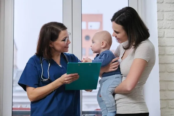 Doctor pediatrician talking with young mother holding her baby in her arms Stock Image