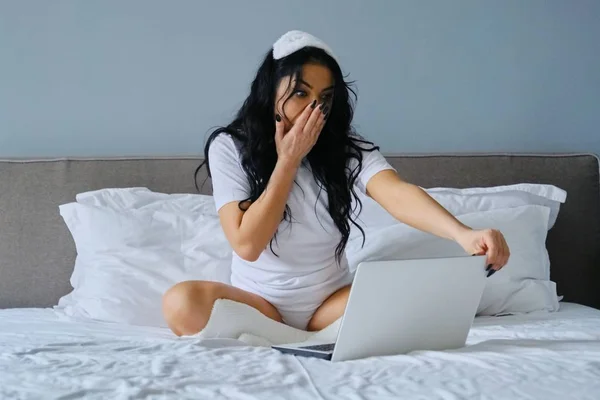 Красива емоційна жінка сидить у ліжку за допомогою портативного комп'ютера — стокове фото