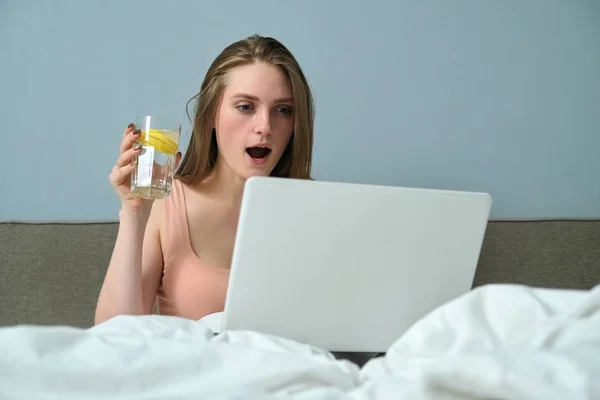 Красива емоційна жінка сидить у ліжку за допомогою портативного комп'ютера — стокове фото