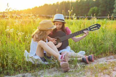 Çocuklar klasik gitarla doğada oturuyor.