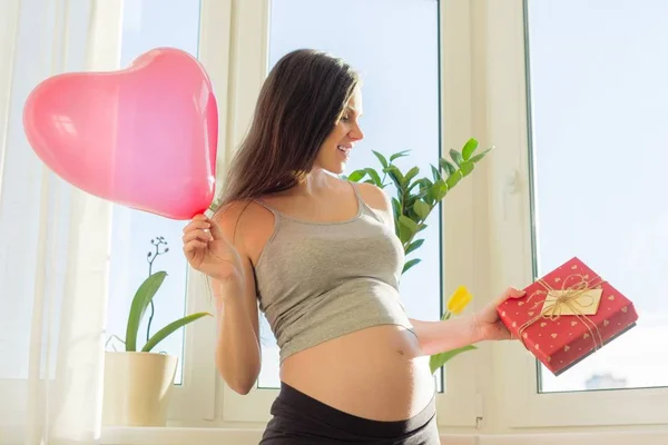 Happy young pregnant woman with gift box and heart balloon — Stock Photo, Image