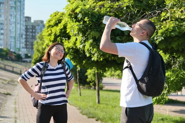 Dojrzały mężczyzna i kobieta z plecakami spacerujących w parku rozmawiających wody pitnej — Zdjęcie stockowe