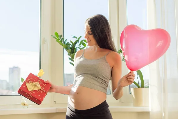 Joven mujer embarazada hermosa con caja de regalo y corazón de globo —  Fotos de Stock