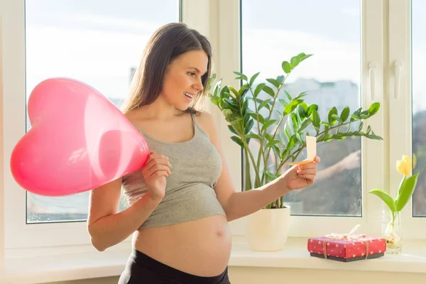 Happy pregnant female with Valentines gift box and red heart balloon — Stock Photo, Image