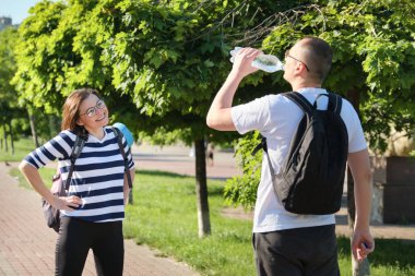 Sırt çantalı olgun bir adam ve kadın parkta yürüyüp içme suyu hakkında konuşuyorlar.