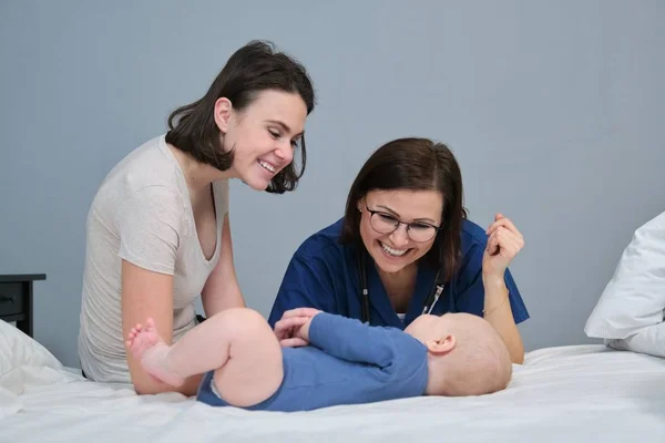 Pediatra de uniforme azul com estetoscópio conversando com a jovem mãe do bebê — Fotografia de Stock