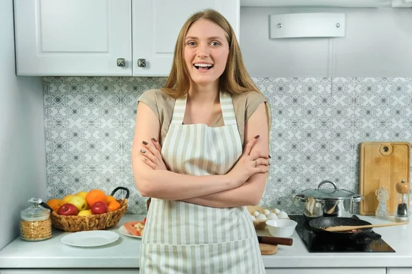 Jonge vrouw in schort met gevouwen armen thuis in de keuken — Stockfoto