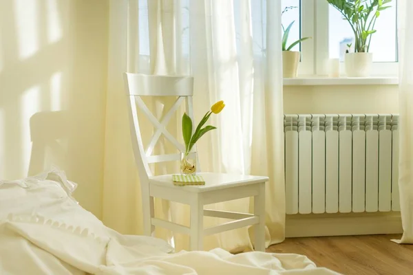 Jasna wiosna sypialnia wnętrze, łóżko, białe krzesło, szkło z żółtym tulipanem — Zdjęcie stockowe
