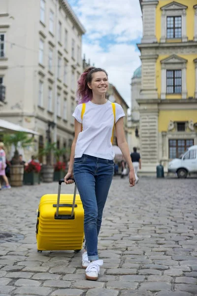 Menina adolescente andando com mochila e mala amarela na rua da cidade — Fotografia de Stock