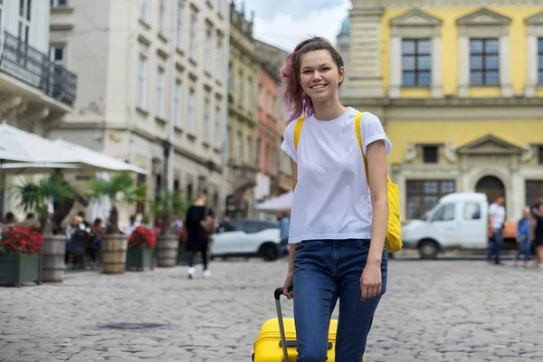 Meisje tiener wandelen met rugzak en gele koffer op straat — Stockfoto