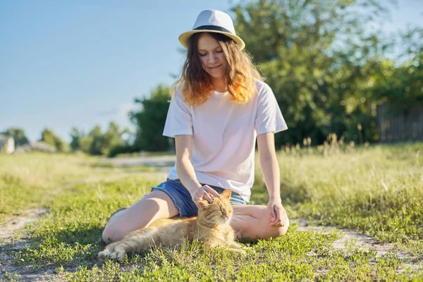 Teenager dívka v klobouku na přírodě hrát s červenou kočkou, rustikální styl — Stock fotografie