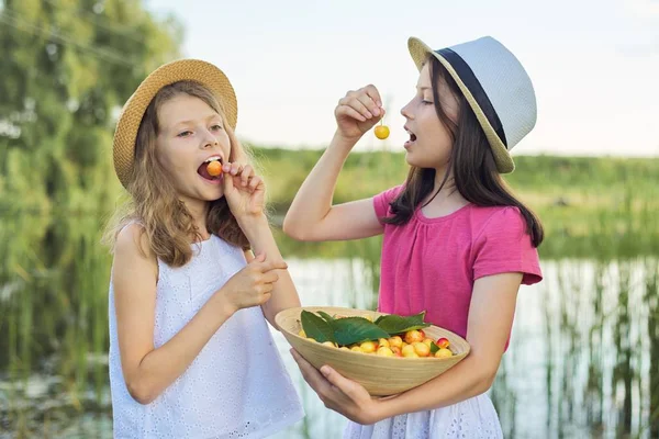 Dvě dívky jedí žluté třešně, letní den v přírodě — Stock fotografie