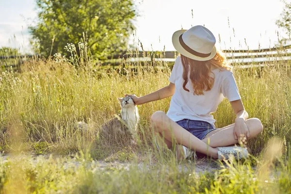 Ragazza adolescente in cappello sulla natura che gioca con il gatto grigio soffice, campagna — Foto Stock