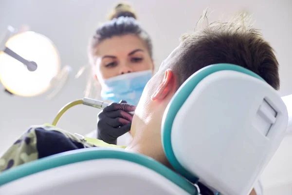 Dentista femenina tratando dientes a paciente, joven en silla en clínica dental — Foto de Stock