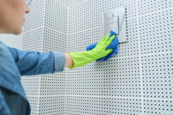 Vrouw schoonmaken en polijsten chroom toilet knop op betegelde muur — Stockfoto