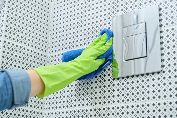 Woman cleaning and polishing chrome toilet button on tiled wall — 스톡 사진
