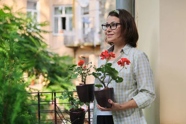 Mooie volwassen vrouw met potted rode zomer bloemen — Stockfoto