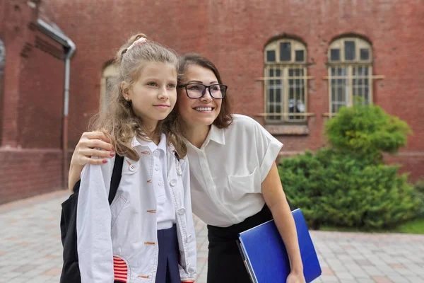 Учитель обнимает ребенка возле школьного здания. Возвращение в школу, начало занятий — стоковое фото