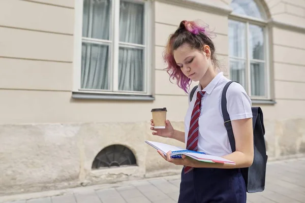 Niña estudiante de 15, 16 años caminando con mochila, leyendo cuaderno y bebiendo — Foto de Stock