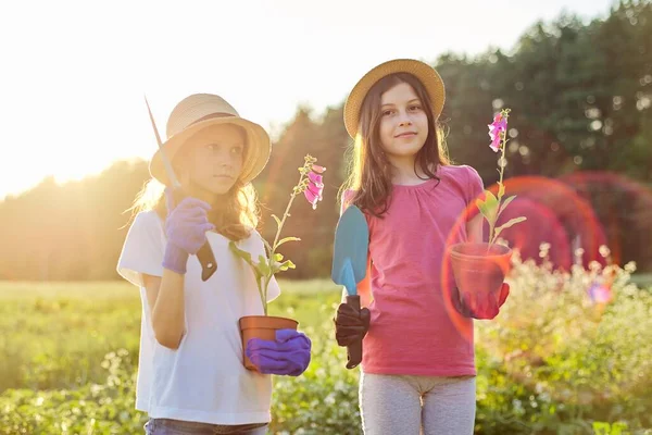 Retrato de dos pequeños jardineros en guantes con plantas con flores en macetas y palas de jardín — Foto de Stock