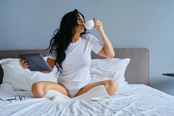 Красива брюнетка сидить у ліжку за допомогою цифрового планшета — стокове фото