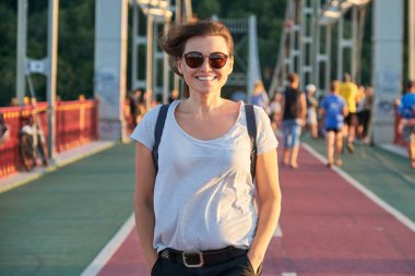 Outdoor portrait of happy smiling mature woman in sunglasses walking on bridge