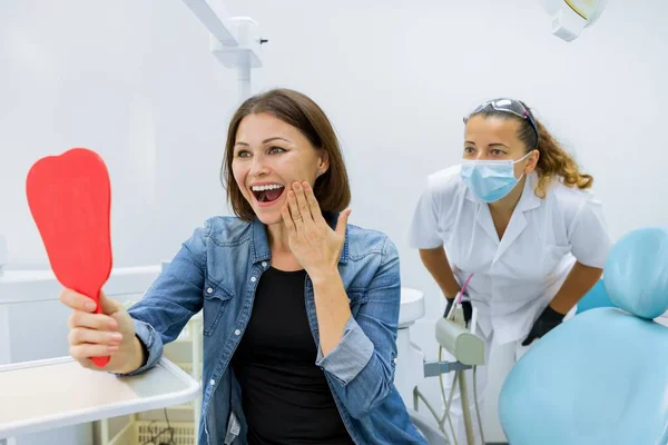 Szczęśliwa dojrzała kobieta po leczeniu i protezach patrząc w lustro na zęby — Zdjęcie stockowe